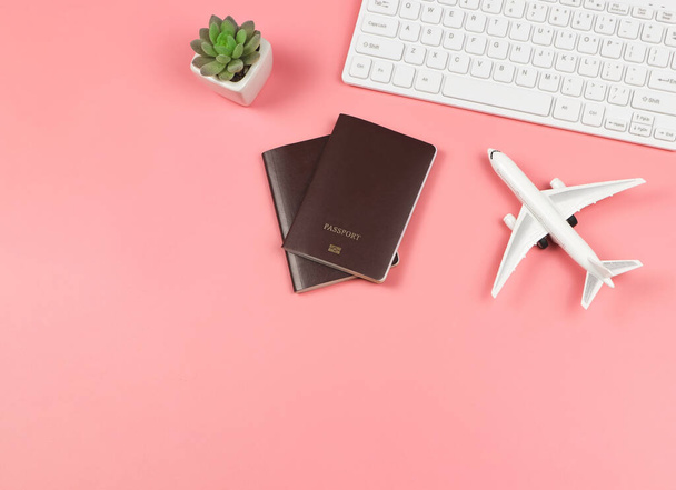 Bovenaanzicht of platte lay-out van vliegtuig model, computer toetsenbord, twee paspoorten en cactus op roze achtergrond, business en reizen concept. - Foto, afbeelding