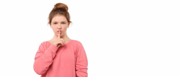 niña de 12-14 años de edad manteniendo el dedo índice cerca de la boca haciendo señal de silencio, decir shhh, aislado sobre fondo blanco. Concepto secreto, expresión y emoción - Foto, Imagen
