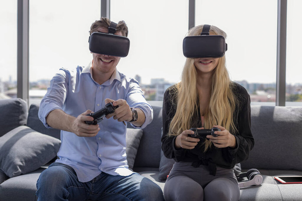 Young couple sitting on the floor at home. Portrait of wife and husband have fun playing video games with joystick and VR. stay at home. - Photo, Image