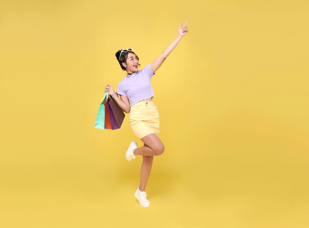 Fröhlich glücklich Teenager asiatische Frau beim Einkaufen, trägt sie Einkaufstüten und zeigt mit dem Finger auf die neuesten Angebote im Einkaufszentrum zu bekommen. - Foto, Bild