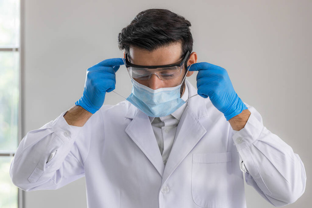 Close up male doctor, researcher, scientist wearing eye protection glasses, white suit, glove and mask on grey background. Healthcare and medical concept. - Фото, изображение