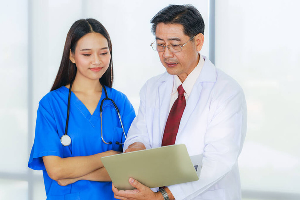 Старший азіатський лікар в окулярах з ноутбуком і молода жінка лікар зустрічаються в кімнаті для зустрічей в лікарні.. - Фото, зображення