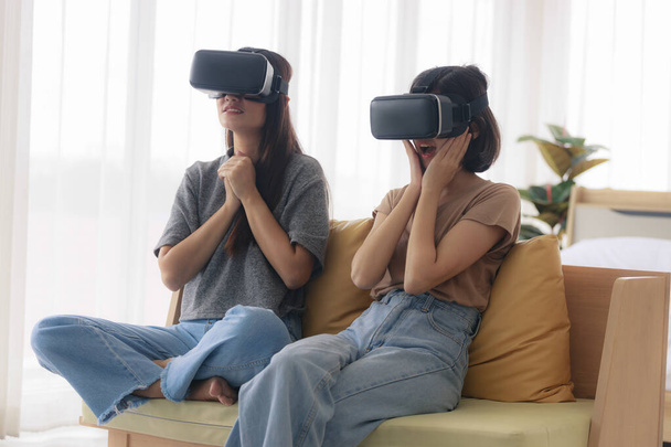 Due adolescenti asiatiche sono amiche intime con i capelli corti e lunghi che indossano occhiali VR per giocare e guardare un film o un intrattenimento in camera da letto. Giovani donne stanno godendo di attività ricreative - Foto, immagini