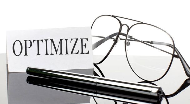 Texto OPTIMIZAR sobre papel adhesivo blanco sobre fondo claro con bolígrafo y gafas. Negocio - Foto, Imagen