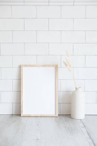 Photo frame mockup and vase of dried flowers on table. Brick tiles wall on background. Scandinavian, nordic style. Interior design. - Photo, image
