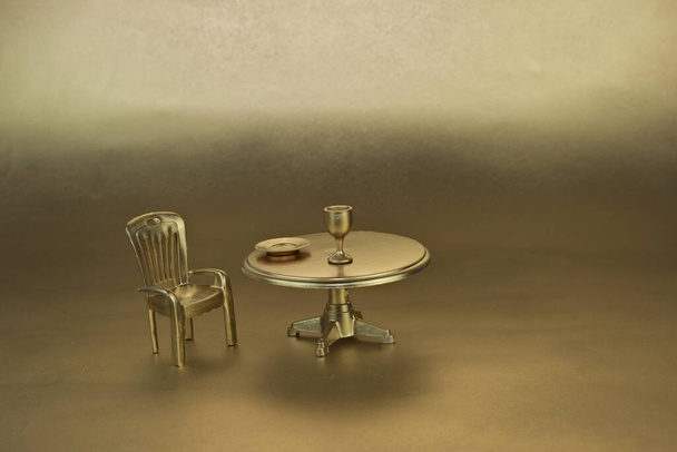 The miniature figurines of golden chair, table and tableware isolated in golden background - Fotó, kép