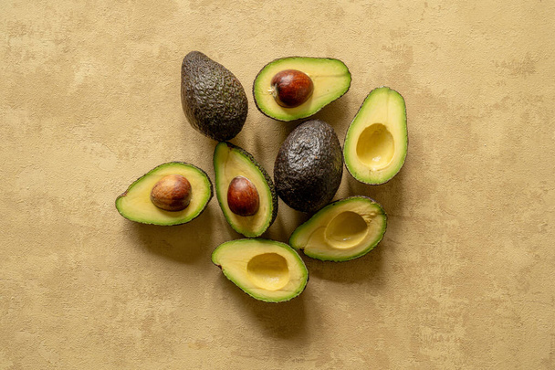 A creative top view of sliced and whole avocados on a textured beige background - Foto, Imagem