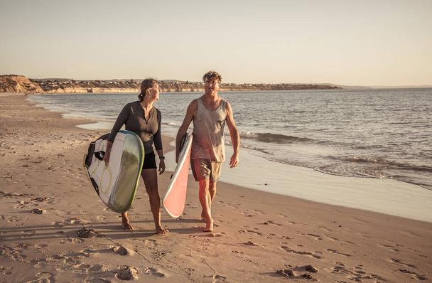 Mature couple with surfboards on beautiful beach enjoying paradise and active lifestyle. Attractive fit man and woman surfing and having fun. In travel, active healthy people and outdoors sports. - Fotoğraf, Görsel
