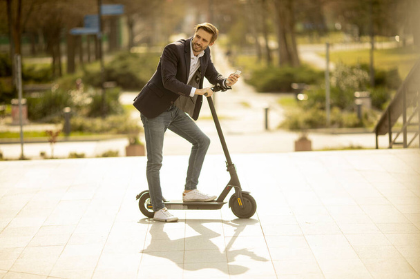 Handsome young businessman using mobile phone  on electric scooter - Photo, Image