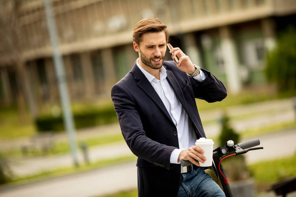 Beau jeune homme d'affaires utilisant le téléphone mobile sur scooter électrique - Photo, image
