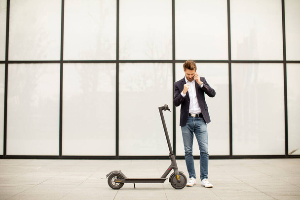 Bonito jovem empresário usando telefone celular em scooter elétrico - Foto, Imagem