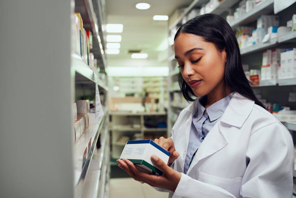 Young female pharmacist reading instructions on medicine box standing in aisle of chemist - Φωτογραφία, εικόνα