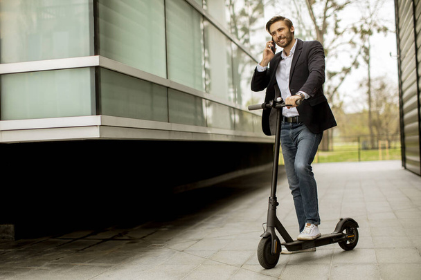 Bello giovane uomo d'affari che utilizza il telefono cellulare su scooter elettrico - Foto, immagini