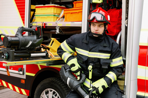 A man of strong physique in uniform and helmet stands by a rescue vehicle. Man rescuer - Fotoğraf, Görsel