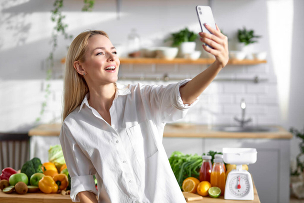 happy female diettian with smartphone in hands in kitchen - Photo, image