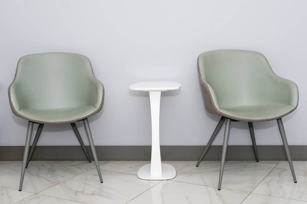 Vista frontal de sillas modernas y sencillas contra la pared gris en un interior de sala de espera de estilo minimalista. Sillas en la sala de espera del consultorio del médico con espacio para copiar el texto - Foto, Imagen