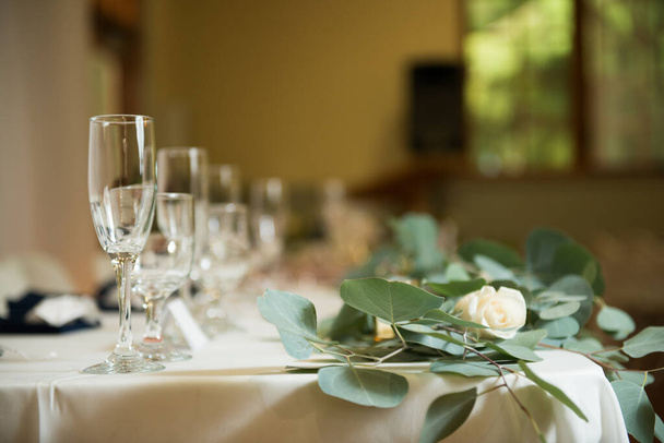 A closeup shot of a line of glasses with water and white roses on a long, white table - Photo, Image