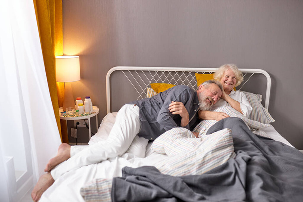 positive caucasian elderly couple have fun. laugh while lying on bed at home - Zdjęcie, obraz