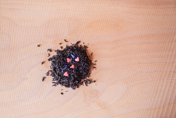 té negro con corazones rosados en una tabla de madera, bebida elaborada aromática seca, té de hierbas en primer plano a granel - Foto, Imagen