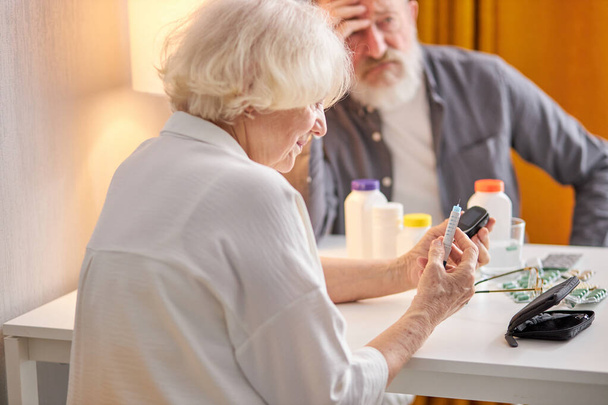 Senior hands with glucometer in hands and pills and drugs on table, checking blood sugar - Foto, immagini