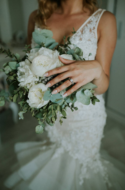 Um tiro vertical de noiva vestindo o vestido de noiva e anel de casamento segurando um belo buquê - Foto, Imagem
