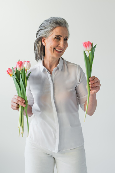 gai mature femme regardant tulipe isolé sur gris  - Photo, image