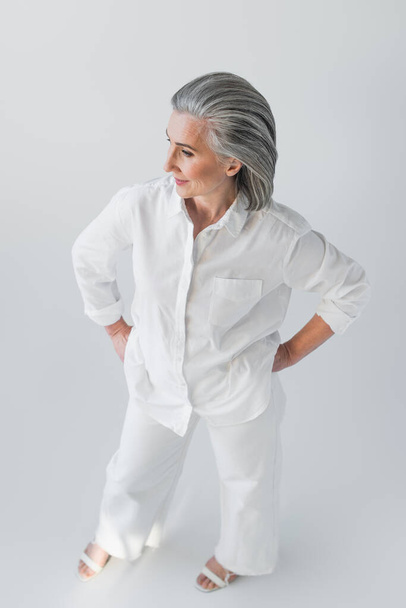 Overhead view of mature woman standing with hands on hips on grey background  - Foto, Imagem