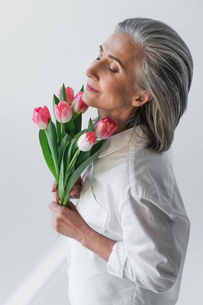 Mujer madura sosteniendo tulipanes aislados en gris  - Foto, Imagen