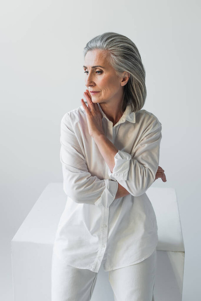 Mature woman looking away near cube isolated on grey  - Foto, imagen