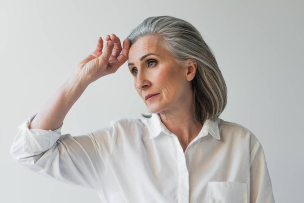 Middle aged woman with hand near forehead isolated on grey  - Valokuva, kuva