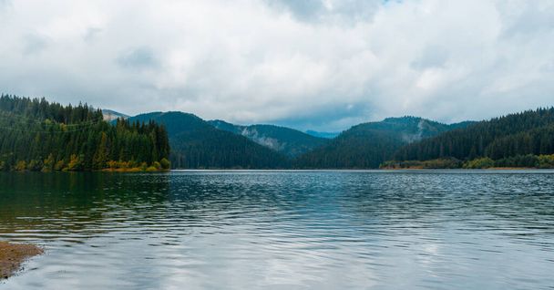A beautiful scenery of a lake surrounded by rocky mountains under a cloudy sky in Romania - Valokuva, kuva
