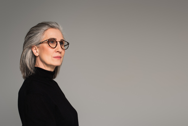 Mature woman in eyeglasses looking away isolated on grey  - Fotó, kép