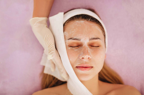 Dermatologue professionnel utilisant une serviette cosmétique pour nettoyer le visage féminin. L'esthéticienne retire le masque du visage du patient. Gros plan.  - Photo, image
