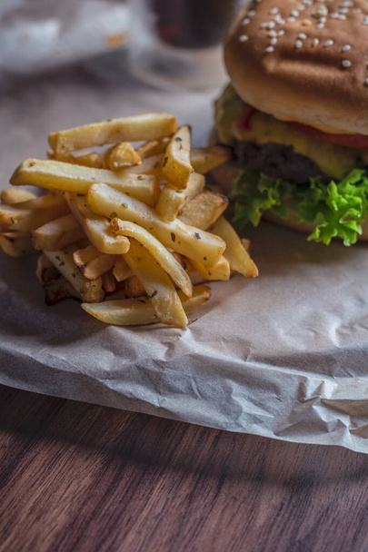 Hambúrguer caseiro e batatas fritas com orégano e vidro congelado um refrigerante saboroso. Humburger servido em papel pergament e tábua de madeira. Fechar.  - Foto, Imagem