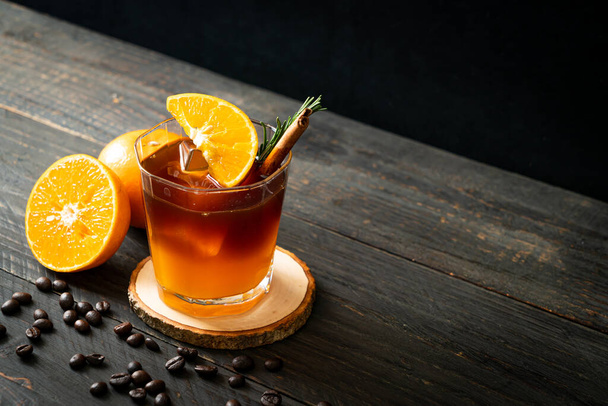 A glass of iced americano black coffee and layer of orange and lemon juice decorated with rosemary and cinnamon - Фото, изображение