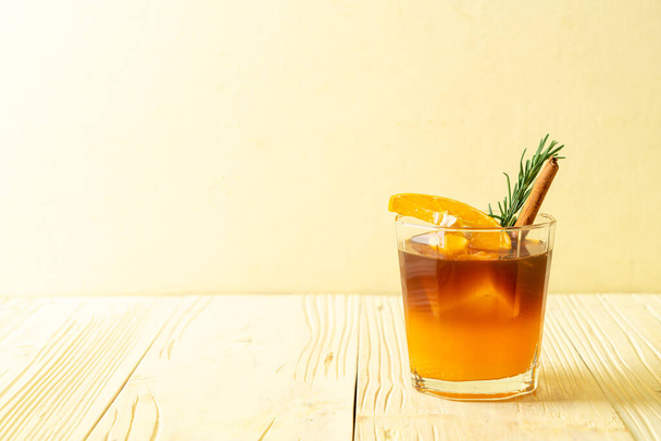 A glass of iced americano black coffee and layer of orange and lemon juice decorated with rosemary and cinnamon - Fotoğraf, Görsel