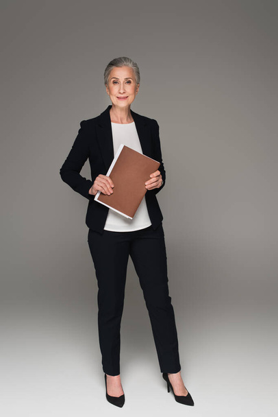 Mature businesswoman holding paper folder on grey background  - Foto, Bild
