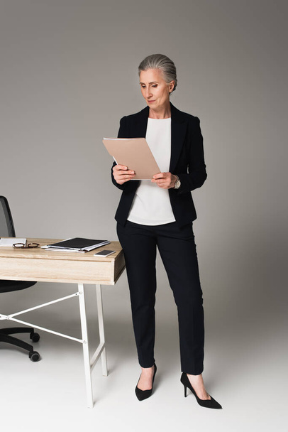 Geschäftsfrau betrachtet Dokumente am Tisch auf grauem Hintergrund  - Foto, Bild