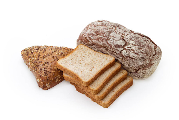 Целая буханка темно-коричневого хлеба с патокой, хлеб треугольной формы, посыпанный различными семенами и несжареными ломтиками хлеба на белом фоне - Фото, изображение