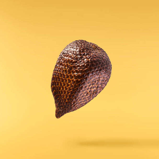 Fresh ripe salak ar snake fruit falling in the air isolated on yellow background. Zero gravity or levitation conception. High quality resolution image - Photo, Image
