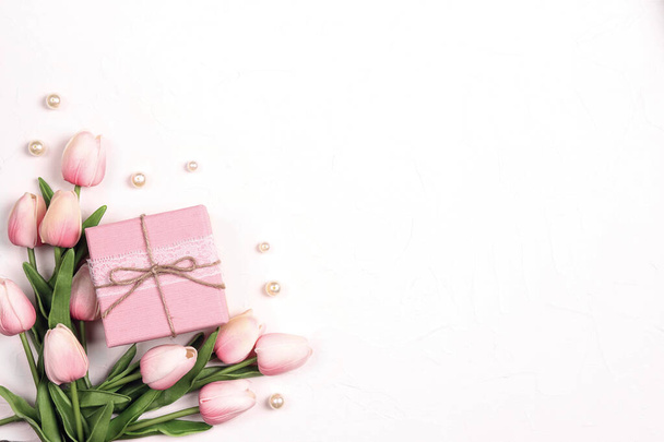 Festive white background with tulip flowers, gift and beads. Top down composition with copy space. Valentine's Day, Mother's Day or 8 March greeting card. - Φωτογραφία, εικόνα