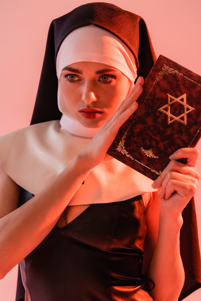 αισθησιακή καλόγρια που κρατάει την Εβραϊκή Βίβλο απομονωμένη στο ροζ - Φωτογραφία, εικόνα