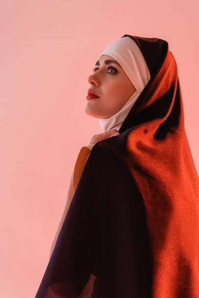 jovem freira em vestimenta preta olhando para longe isolado em rosa - Foto, Imagem
