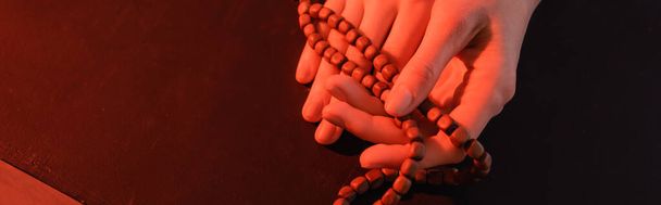 przycięty widok rąk zakonnicy z paciorkami modlitewnymi na czarnej powierzchni, sztandar - Zdjęcie, obraz