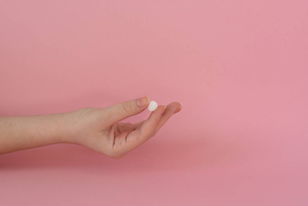 Витаминные таблетки в руке женщины, розовый фон - Фото, изображение