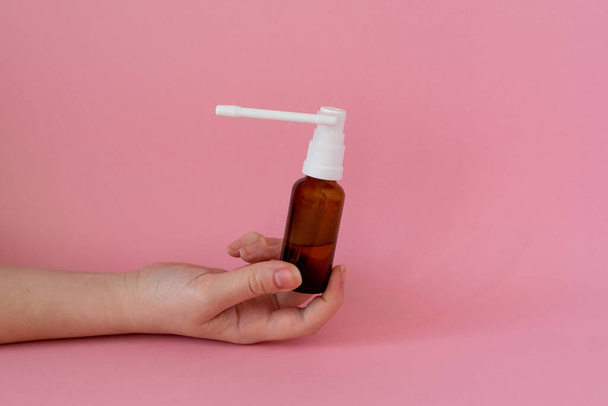 Бутылка с лекарственным горловым спреем в руке, розовый фон - Фото, изображение