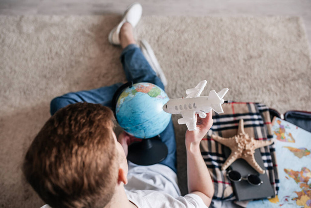 guy sitting on the floor at home with a suitcase, planning a trip, buying tickets online, traveling dreams - Фото, изображение