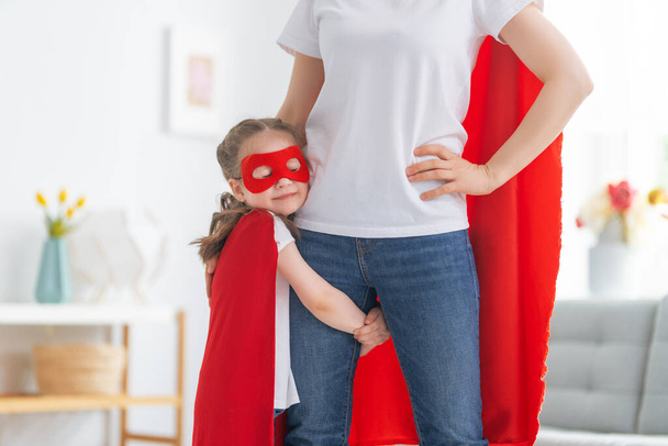 Mother and her child playing together. Girl and mom in Superhero costume. Mum and kid having fun. Family holiday and togetherness. - Foto, afbeelding