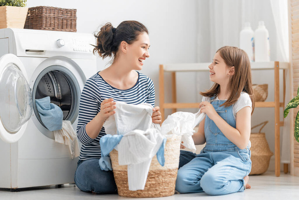 美しい若い女性と子供の女の子の小さなヘルパーは家で洗濯をしながら楽しさと笑顔を持っています. - 写真・画像