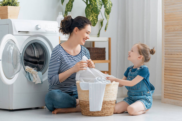 Beautiful young woman and child girl little helper are having fun and smiling while doing laundry at home. - Fotografie, Obrázek